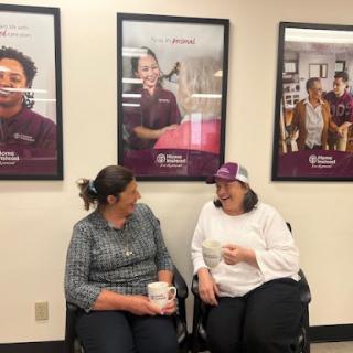 Two women engaged in a friendly conversation in an indoor space with posters in the background.