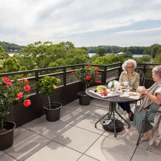 Two people enjoying a conversation on a scenic balcony with flowers and a view of the lake.