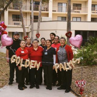 A team gathered outdoors holding a 'Golden Palms' banner, surrounded by heart-shaped balloons.