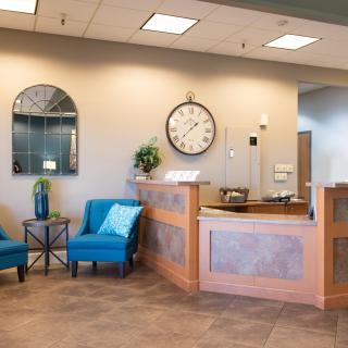 A welcoming reception area with blue chairs and a large wall clock.