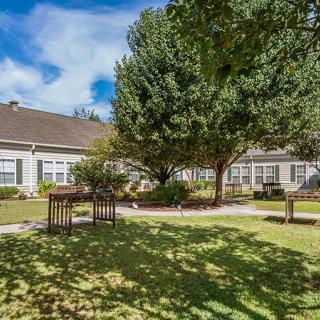 A peaceful garden scene with lush trees and a well-maintained building under a clear blue sky.
