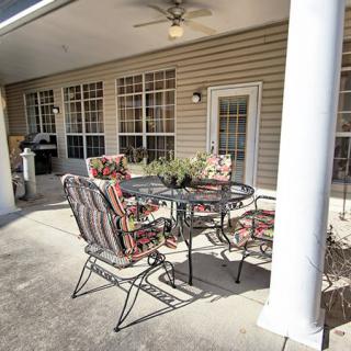 A cozy outdoor patio area with a metal table and cushioned chairs, accompanied by a ceiling fan, set against the backdrop of a house exterior with glass doors.