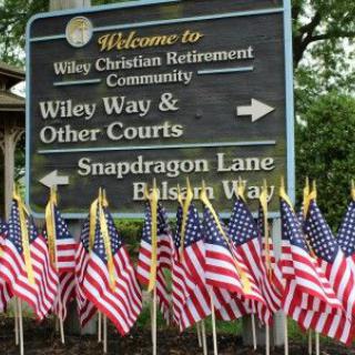 A directional sign at Wiley Christian Retirement Community, adorned with American flags, indicating directions to various courts and lanes.
