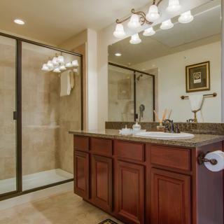 A well-appointed bathroom featuring a glass-enclosed shower, a large mirror above the sink, and elegant lighting fixtures.