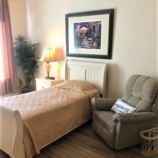 A cozy bedroom with a single bed, comfortable armchair, and warm lighting from a table lamp.