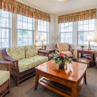 A cozy living room with wicker furniture, large windows, and floral curtains.