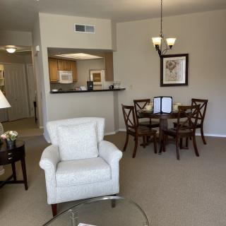A cozy living room with an armchair, a dining table with chairs, and an open view of the kitchen.