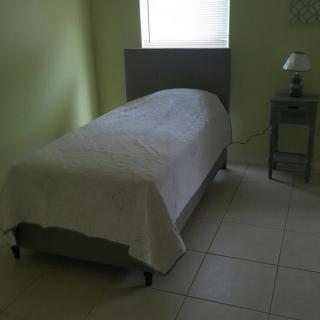 A minimalist bedroom with a single bed, nightstand, and lamp near a window.