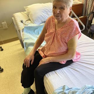 A woman sitting on the edge of a hospital bed, dressed in casual clothing.