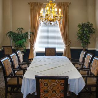 A formal dining room with a long table, surrounded by chairs, adorned with a chandelier and elegant curtains.