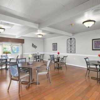 A spacious dining area with multiple tables and chairs, featuring a hardwood floor and decorative wall art.
