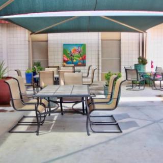 An outdoor patio area with tables, chairs, and potted plants under a shade canopy.