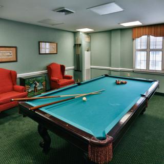 A cozy billiards room featuring a pool table, red armchairs, and a window with drapes.
