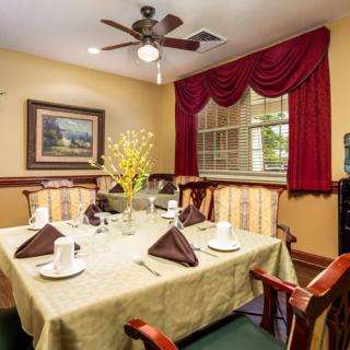 An elegantly set dining table in a cozy dining room with a ceiling fan and red drapes.
