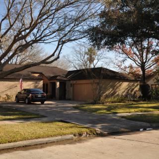 A suburban house with a car parked in the driveway, surrounded by trees.
