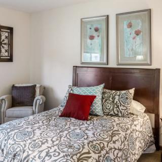 A cozy bedroom with a patterned bedspread, decorative pillows, and framed artwork on the wall.
