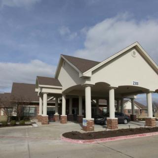 A large building with a covered entrance, featuring columns and a driveway under a partly cloudy sky.