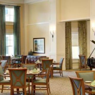 A spacious dining area with neatly arranged tables and chairs, featuring a piano in the corner.