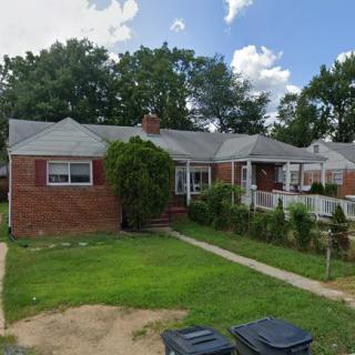 A suburban brick house with a well-maintained lawn and surrounding trees.