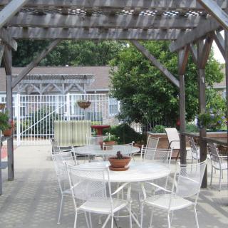 A peaceful patio area with a pergola, featuring white garden furniture and potted plants.