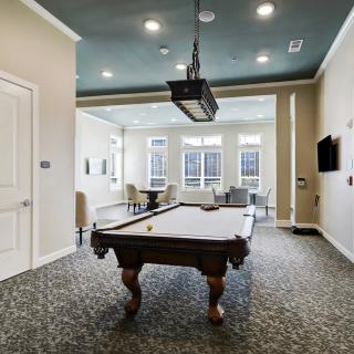 A modern game room featuring a pool table, stylish lighting, and a cozy seating area by the windows.