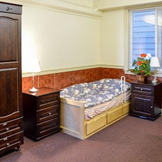 A cozy bedroom with a bed, wardrobe, nightstands, and a window with a flower pot.