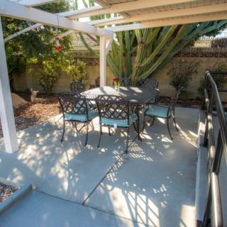 A cozy outdoor patio area with a table and chairs under a pergola, surrounded by garden plants.