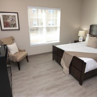 A cozy bedroom featuring a neatly made bed, a comfortable chair, and a large window allowing natural light to brighten the space.