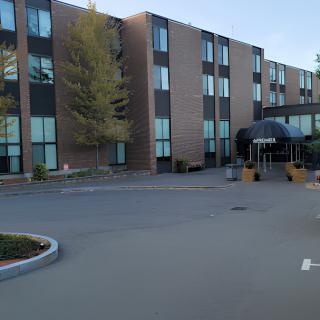 A modern hotel building with a spacious parking lot and surrounding trees.