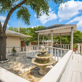 A sunny patio with a fountain and a pergola surrounded by trees.