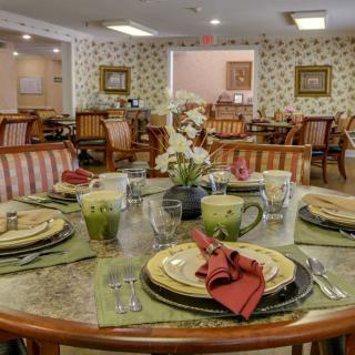 A warmly decorated dining room with elegantly set tables, featuring floral arrangements and neatly arranged tableware.