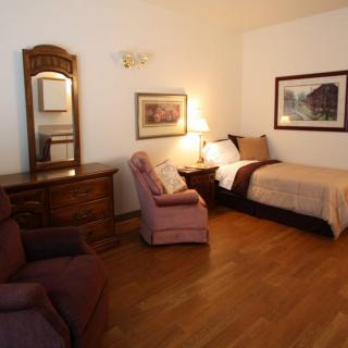 Cozy bedroom with a single bed, armchairs, and classic wooden furniture.