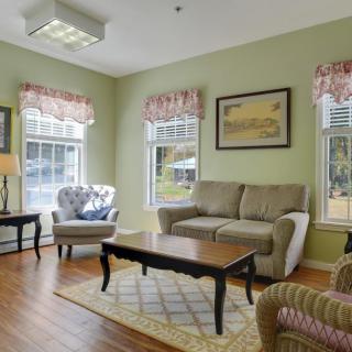 Cozy living room with a sofa, armchair, and coffee table surrounded by windows and decorated with wall art.