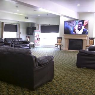 A cozy living room with leather couches, a large TV above a fireplace, and carpet flooring.