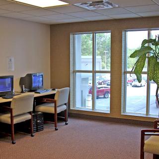 A small office area with two computer stations, chairs, large windows, and an indoor plant.