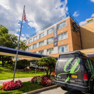 A hotel entrance with a parked van, surrounded by landscaped gardens and an American flag flying on a sunny day.