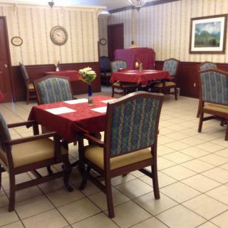 An empty restaurant dining area with neatly arranged tables and chairs, featuring red tablecloths and a wall clock.
