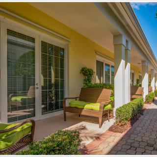 A sunny patio with comfortable seating and green cushions against yellow walls.