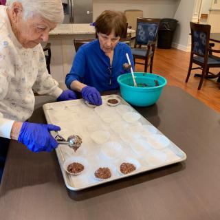 A senior and a child are baking cookies together in the kitchen, placing dough on a tray.