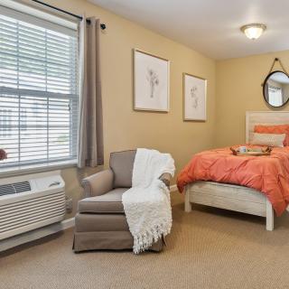 A cozy bedroom with an armchair and a neatly made bed in warm tones.