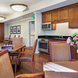 A cozy dining area with wooden furniture and a kitchenette in the background, featuring flowers on the table.