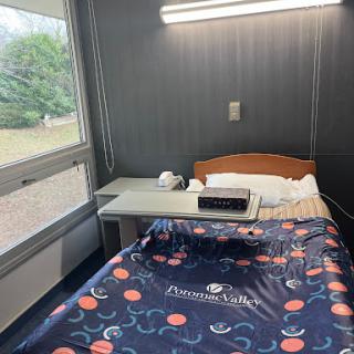 A well-lit hospital room featuring a single bed, a small bedside table, and a window with a view.