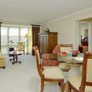 A cozy living room with a traditional style, featuring a dining area and large windows.