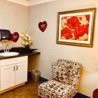 A cozy room featuring a patterned chair, sink area, and floral wall art with heart decorations.