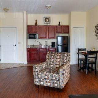 A cozy living space featuring a patterned armchair, a kitchenette with red cabinets, and a small dining area.