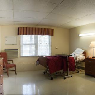 A view of a hospital room featuring a bed, chair, and window with curtains.