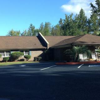 A single-story building with a sloped roof surrounded by trees and an adjacent parking lot.