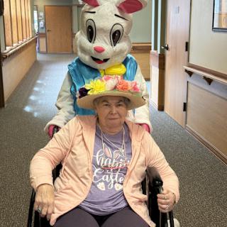 An elderly woman enjoys a joyful moment with a rabbit mascot during a spring celebration at the care facility.