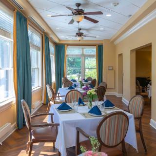 A well-lit dining room with elegant table settings, surrounded by large windows and blue curtains.