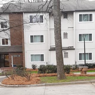 A view of a residential apartment building with a tree and parking area in the foreground.